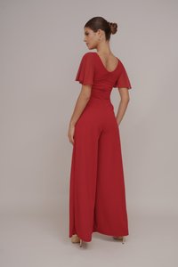 Rode jumpsuit met fladdermouwen, een diepe V-rug en wijde benen. Zachte stof met een gladde textuur. Minimalistische stijl; ritssluiting aan de achterkant.