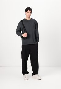 Long-sleeve dark gray shirt, loose black cargo pants with pockets, white sneakers, and a black shoulder bag. Simple and casual design.
