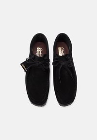 Scarpe nere in suede con punta arrotondata, allacciatura frontale e cuciture visibili. Etichettate "Clarks Originals" sulla soletta. Senza fantasie o accenti.