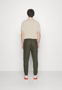 Beige Polo-Shirt mit kurzen Ärmeln, olivgrüne Cargo-Hosen mit elastischem Bund und Gesäßtaschen, kombiniert mit Turnschuhen mit roten Akzenten.