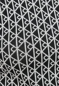 Zwarte stof met een wit geometrisch patroon van in elkaar grijpende driehoeken en lijnen, met een textuur van gebreide oppervlakte.