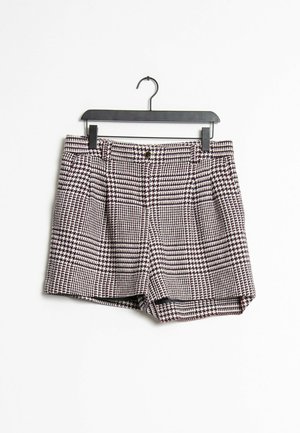 Sort-hvide shorts med hundetandsmønster, knap og bæltestropper, hængende på en sort bøjle mod en hvid baggrund.