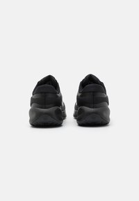 Chaussures de sport noires avec une tige en mesh, un col rembourré et une semelle en caoutchouc. Présente un design minimaliste avec des rayures texturées contrastantes.