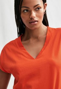 Orange V-hals t-shirt med korte ærmer, lavet af glat stof. Har en afslappet pasform og minimale syninger.
