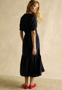 Tumesinine puuvillane kleit kihilise äärega, lühikeste punnpüksi varrukatega ja liibuv vöökoht. Kantud punaste lapikute kingadega, millel on lipsu detail.