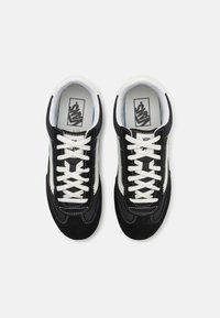 Svart mocka- och lädersneakers med vita snörningar och sidodetaljer. Har en rund tå och kontrasterande sömdetalj.