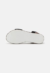 Svart sandal sula med texturerad vit gummi, spårig mönster och vävda detaljer längs kanterna. Platt design för komfort och stabilitet.