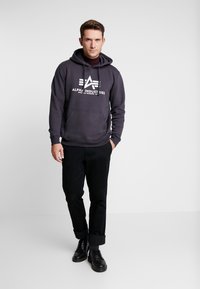 Sudadera gris con bolsillo frontal y logo, combinada con pantalones negros y botas negras de cordones. La sudadera cuenta con cordones y puños acanalados.