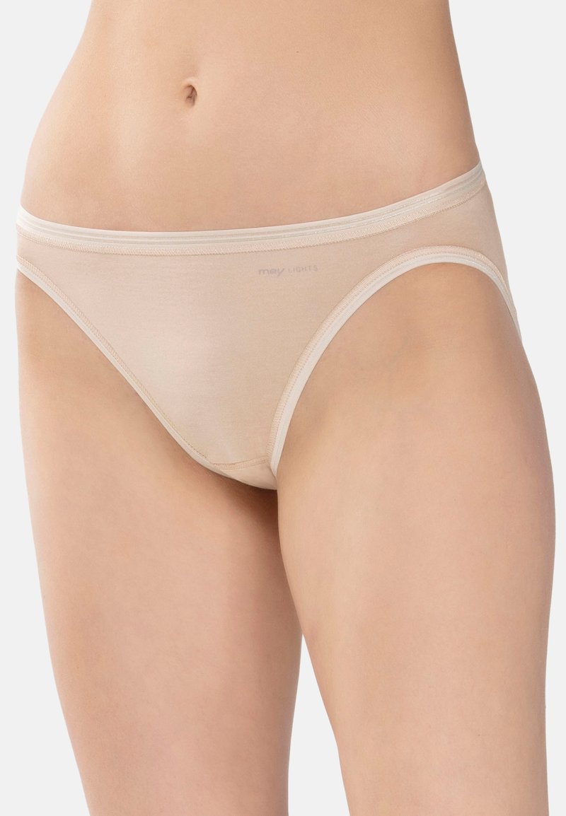 Läheltä otettu kuva henkilöstä, joka on pukeutunut beigeihin alhaisiin puuvillaisiin alusvaatteisiin, joissa on pieni "mey LIGHTS" -logo etuhaarassa.