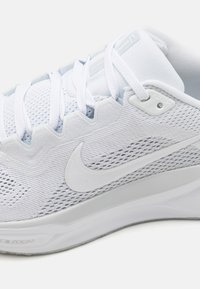 Lekki biały but sportowy z siateczkową górą, teksturowanymi detalami i logo Nike Swoosh. Posiada zapięcie na sznurowadła oraz amortyzowaną podeszwę.