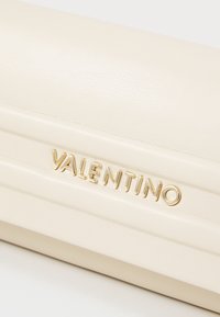 Beżowa skórzana kopertówka o gładkiej fakturze, z złotym logo "VALENTINO" i poziomymi detalami szwów.