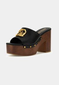 Mule in pelle nera con plateau, tacco a blocco in legno, borchie dorate sui lati e emblema decorativo dorato sulla fascia superiore.