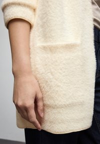 Gräddfärgad, fluffig cardigan med en mjuk textur, med rundad krage och en sidoficka, kombinerad med mörka denim.