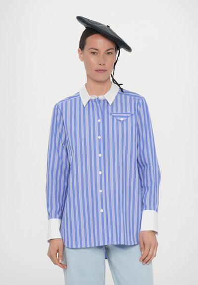 Blue and white striped button-up shirt with a white collar, single chest pocket, and long sleeves. Worn with a black beret hat.
