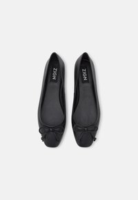 Svarta läderballettskor med rundad tå och en liten rosett i framkant. Slät textur med platt klackdesign.