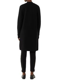 Langer schwarzer Mantel mit gerippter Textur und gerader Schnittführung. Verfügt über einen hohen Kragen und lange Ärmel, kombiniert mit schwarzen Slim-Fit-Hosen und Schuhen.
