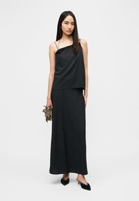 Μαύρο αμάνικο τοπ με ακανόνιστο τελείωμα, συνδυασμένο με μακριά μαύρη φούστα. Αξεσουάρ περιλαμβάνουν τσαντάκι με λεοπάρ μοτίβο και μαύρες μυτερές γόβες.