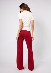 Hvit kortermet topp kombinert med høytlivs, vide røde bukser med en subtil glans. Glatt tekstur og tettsittende silhuett.