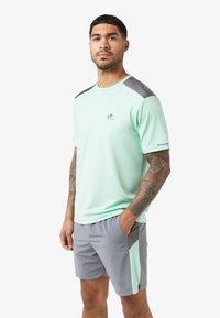 Mintgroene sportshirt met grijze accenten en logo. Korte mouwen, ronde hals, gecombineerd met grijze shorts met zijzakken en bijpassende accenten.