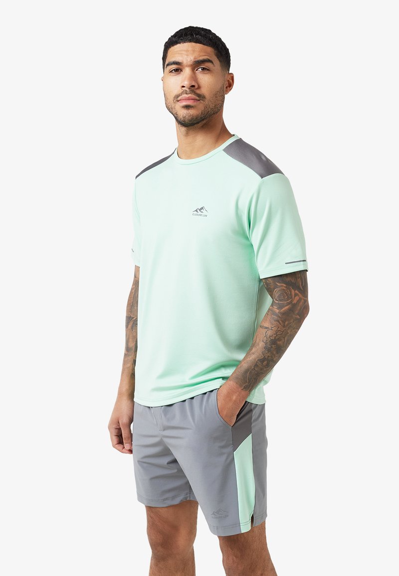 Mintgroene sportshirt met grijze accenten en logo. Korte mouwen, ronde hals, gecombineerd met grijze shorts met zijzakken en bijpassende accenten.