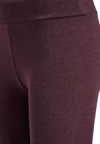 Donkerrode legging gemaakt van rekbare stof, met een gladde textuur en een hoge tailleband, zonder zichtbare naden of patronen.