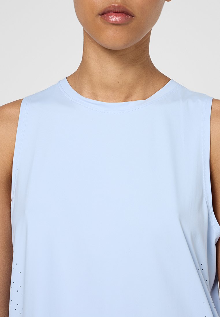 Top sin mangas de color azul claro con cuello redondo, hecho de una tela suave. Presenta pequeñas perforaciones a lo largo de los lados para ventilación.