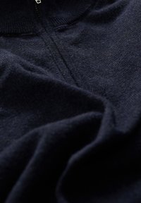 Mörkblå stickad tröja med dragkedja, mjuk textur och ribbad krage. Tyget verkar lätt och något fluffigt.