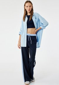Jasnoniebieska, oversize koszula zapinana na guziki noszona na granatowym topie, w zestawieniu z luźnymi granatowymi spodniami z jasnoniebieskimi bocznymi paskami oraz szarymi trampkami.