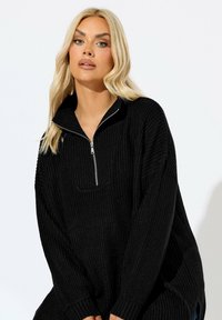 Musta vetoketjullinen villapaita, jossa on teksturoitu neulekuvio, korkea kaulus ja sivurei'ät. Ribbaatut hihansuut täydentävät löysän, ylisuurten siluetin.