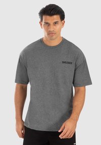 Camiseta de manga corta gris hecha de una mezcla de algodón. Presenta un cuello redondo y un pequeño logo negro "SMILODOX" en el lado izquierdo del pecho.