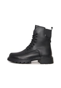 Botas de tobillo negras de cuero sintético, con cordones en la parte delantera, suela de goma gruesa y una tira en la parte posterior. Detalle de superficie texturizada.