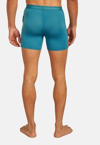 Tealblå boxershorts gjorda av ett mjukt, elastiskt material. Har en mjuk midjeband och en åtsittande design som sträcker sig till mitten av låret.