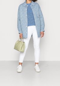 Lichtblauwe bloempatronen oversized shirt, blauwe gebreide trui, witte slim-fit spijkerbroek, witte sneakers, een lichtgroene handtas vasthoudend.