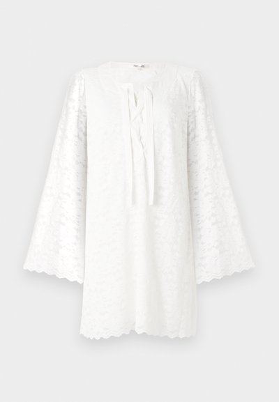 Balta nėriniuota tunika su apvalia iškirpte, ilgomis platėjančiomis rankovėmis ir priekyje rišamu detalumu. Banguotas apdailos kraštas suteikia tekstūros ir vizualinio intereso.