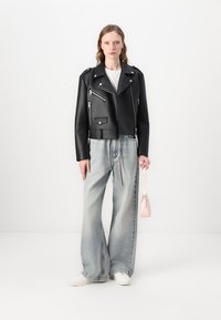 Black leather cropped biker jacket with multiple silver zippers and a breast pocket, paired with light blue oversized denim jeans and white sneakers.