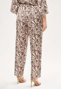 Bruine en crèmekleurige abstracte patroonbroek met een relaxte pasvorm, elastische tailleband en een gladde textuur, gecombineerd met naak hoge hakken sandalen.