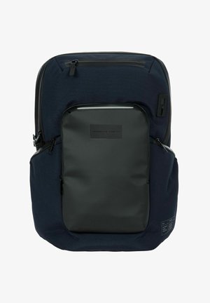 Zaino in tessuto blu navy con una tasca frontale nera opaca. Presenta cerniere, un'etichetta con logo e una striscia riflettente sulla parte superiore.