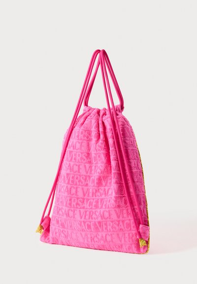 Roza torba svezana vrpcom od plišanog materijala, s utisnutim logotipom "VERSACE", s odgovarajućim ružičastim užetima i zlatnim ukrasnim detaljima.