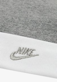 Szürke kötött sapka fehér bordázott szegéllyel és szürke hímzett Nike logóval. Anyaga puha, texturált mintázatú.