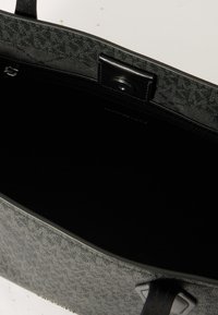 Szara torba na ramię z tkaniny o teksturowanej powierzchni, czarne wnętrze oraz kontrastowe skórzane akcenty na uchwytach i zapięciu.