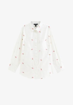 Chemise blanche à manches longues avec boutons, décorée de petites broderies de roses roses dispersées sur le tissu et une poche poitrine unique.