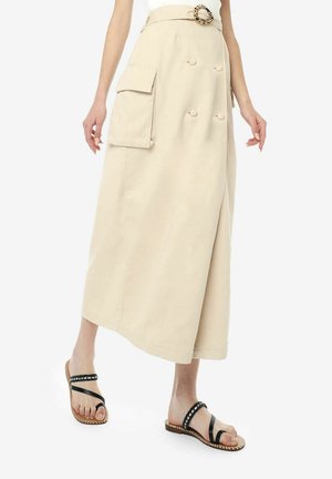 Beige midi-rok gemaakt van zachte stof, met dubbele zijzakken, een aansluitende tailleband en een riemgesp met een cirkelpatroon. Zwarte bandjesandalen.