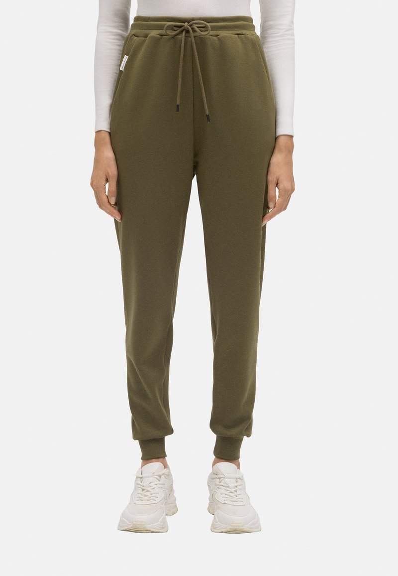 Pantalones de chándal verde oliva con cintura elástica, cordón ajustable, tobillos acampanados y bolsillos laterales. Hechos de una tela suave y texturizada.