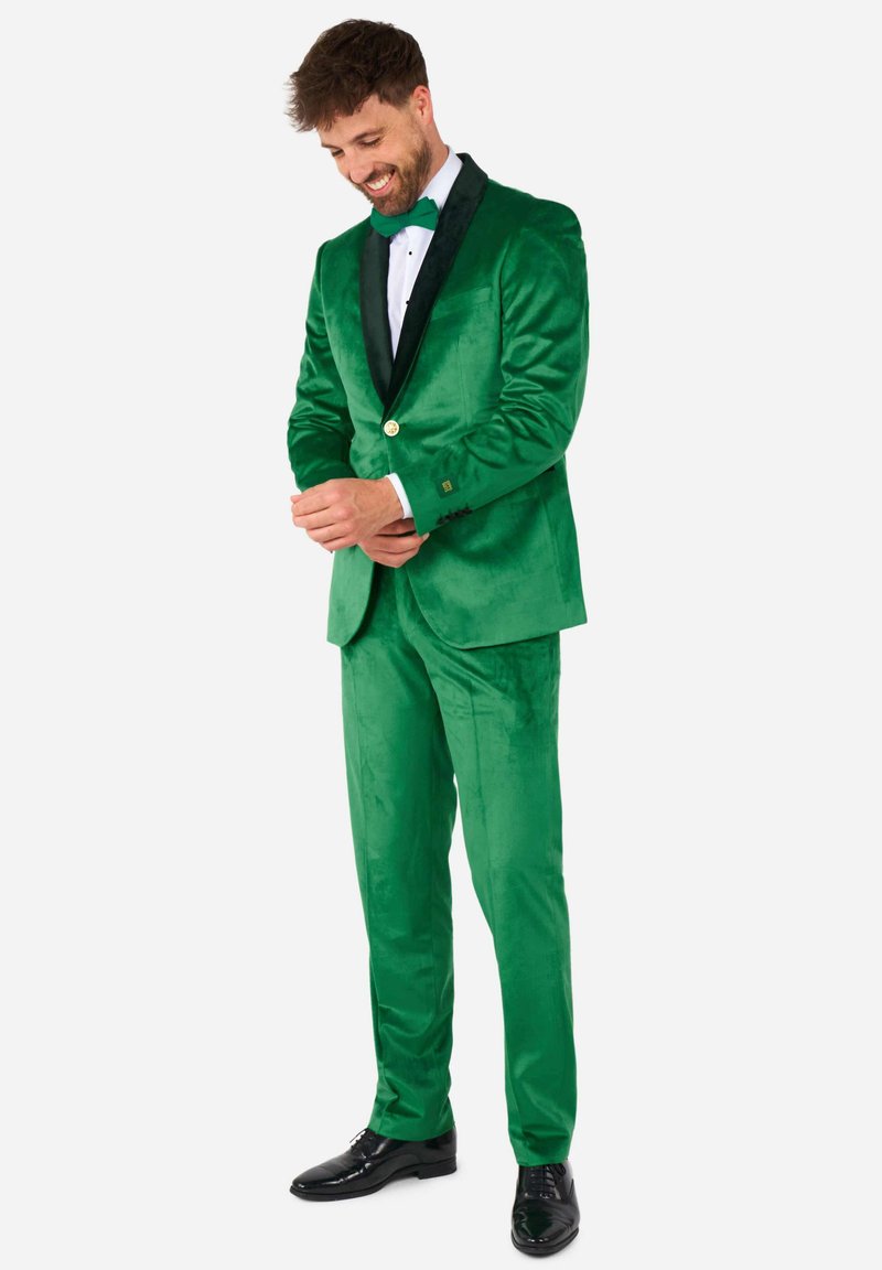 Žalio aksomo kostiumas su juodu aksomo apykakle, auksiniu mygtuku ir derančia kaklaraiščiu. Lygus paviršius, pritaikyta forma, elegantiški juodi batai.