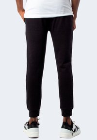 Pantaloni della tuta neri con vestibilità a gamba affusolata, vita elastica e polsini a coste. Indossati con sneaker bianche e nere. Tessuto morbido in misto cotone.