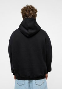 Hoodie noir surdimensionné avec une capuche à cordon de serrage, des poignets et un ourlet côtelés. Matériau doux, présente une arrière uni sans logos ni motifs visibles.