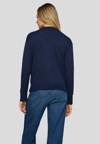 Dunkelblauer gestrickter Pullover mit langen Ärmeln, gerippten Bündchen und Saum hinten. Kombiniert mit blauen Jeans, die ein lässiges Outfit präsentieren.