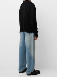 Schwarzer gestrickter Pullover mit geripptem Saum, kombiniert mit hellblauen, weit geschnittenen Jeans mit verwaschenen Stellen und aufgesetzten Taschen. Schwarze Stiefel mit derben Sohlen.