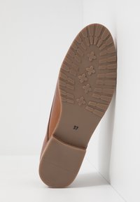 Semelle d'une chaussure en cuir marron avec un motif de bande de roulement composé de grips rectangulaires et en forme de fleur, taille marquée 37 sur la semelle.