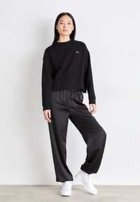 Czarny krótki sweatshirt z prążkowanym dekoltem i małym logo. W połączeniu z luźnymi czarnymi spodniami, stylizowany z białymi sneakersami.